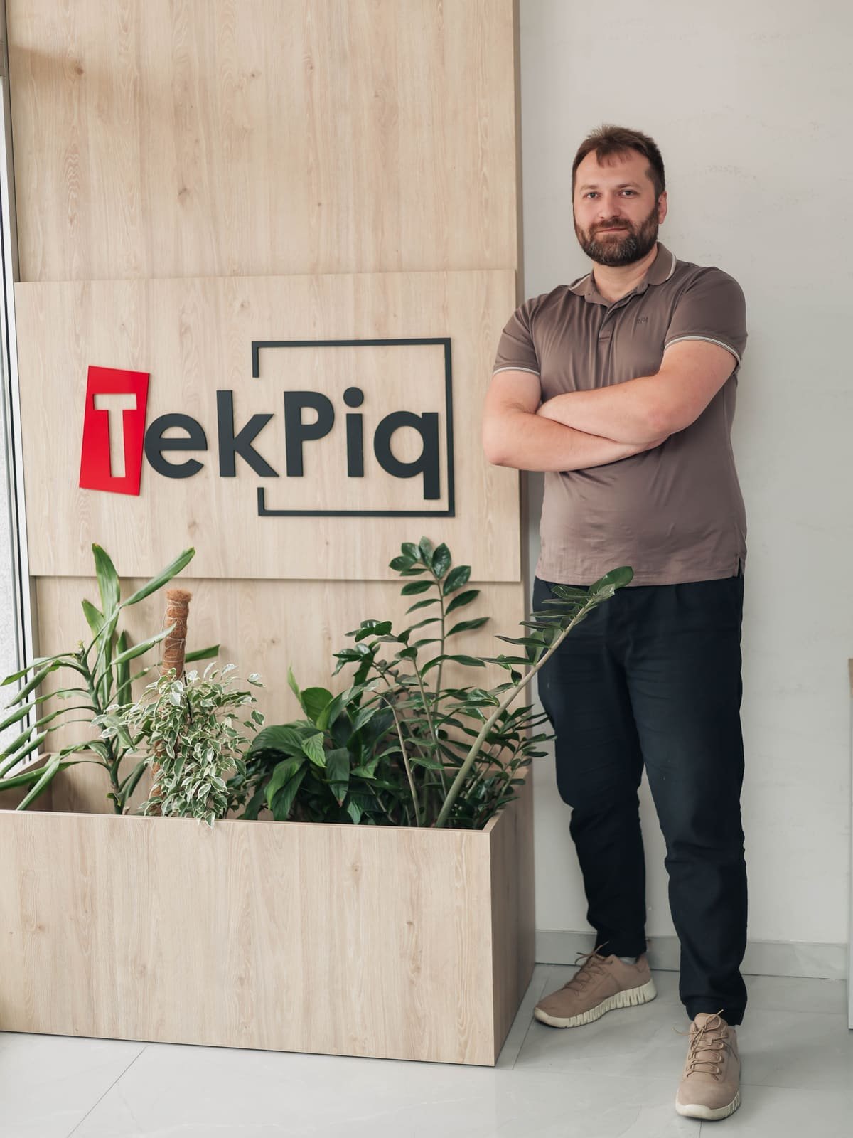 A TekPiq engineer next to the TekPiq logo wall in the office